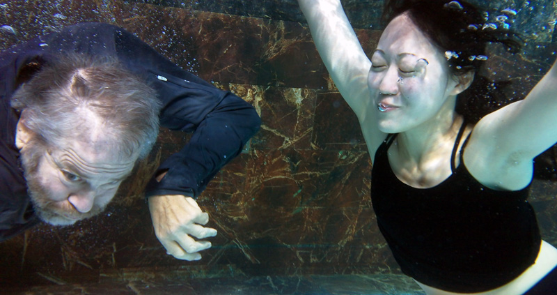 two people, a man and a woman, floating in a marble swimming pool